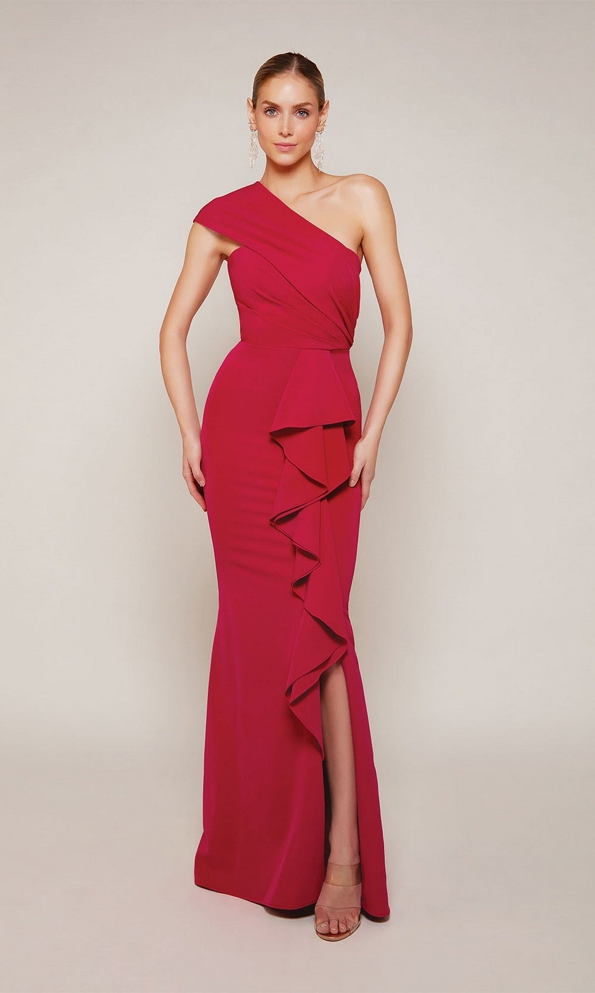 A woman poses elegantly in the Alyce 27646 long formal dress—a magenta one-shoulder sheath style with ruffled details and a thigh-high slit—against a plain background.